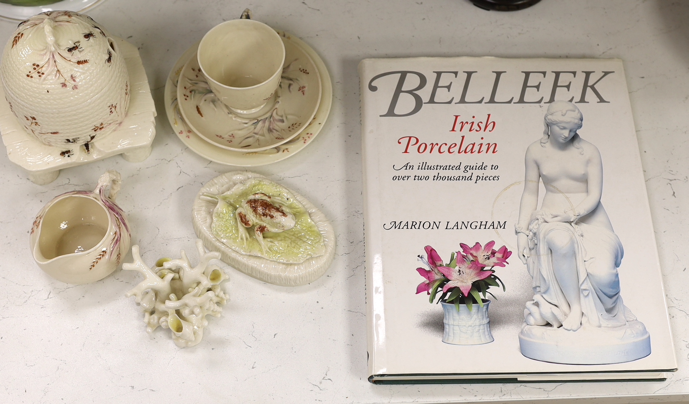 A small quantity of 1st and 2nd period Belleek including a ‘frog’ paperweight and a ‘beehive’ honey jar together with a related reference book by Marion Langham